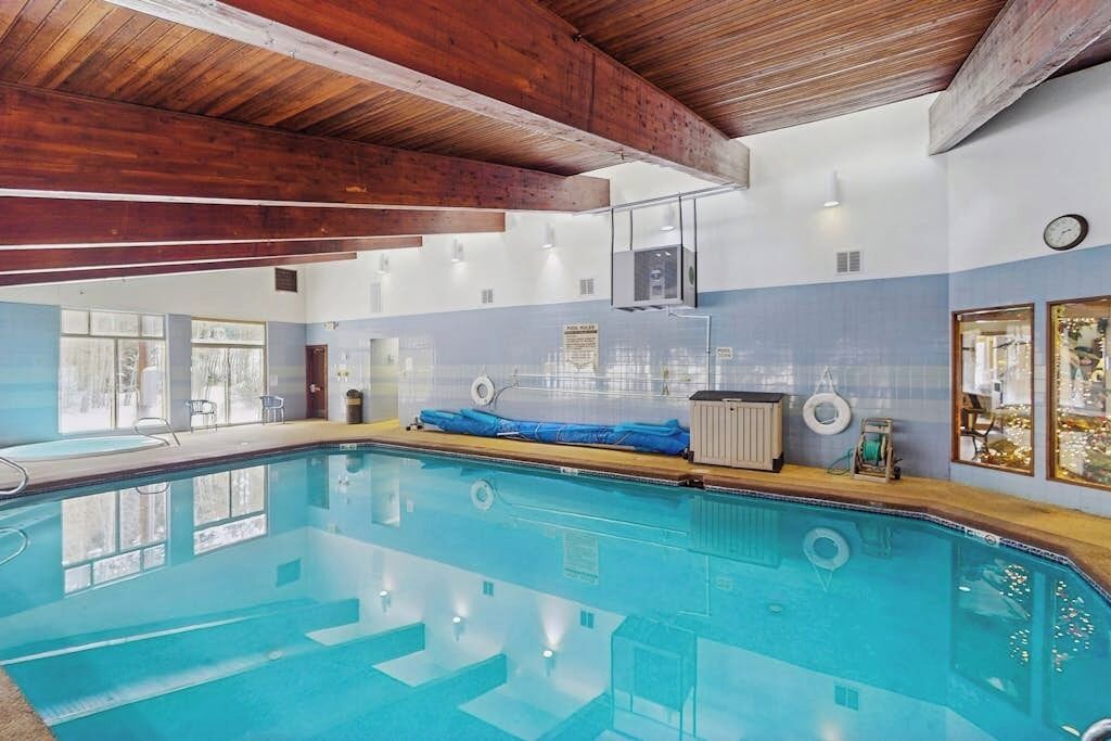 An indoor swimming pool with wooden beams, a blue and white tiled wall, and a clock on the wall.
