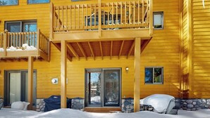 A yellow wooden building with a balcony, a covered patio, and a snow-covered ground.
