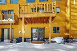 Un bâtiment en bois jaune, doté d’un balcon, d’une terrasse couverte et dont le sol est recouvert de neige.