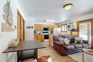 A compact living space with a kitchenette, a brown leather sofa, a dining table, and a wooden floor.