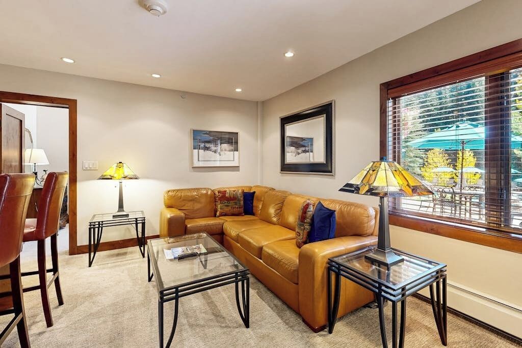 A living room with a leather sofa, glass coffee table, and two lamps.