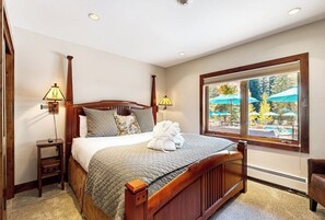 Ein ordentlich bezogenes Bett mit Blick auf ein Außenbecken durch ein großes Fenster.