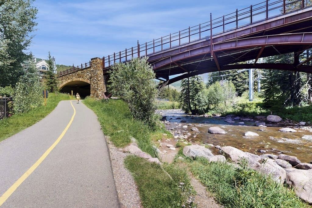 A paved path under a bridge with a stream beside it.