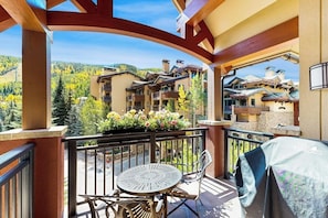 Ein Balkon mit Tisch und Stühlen, einem überdachten Grill und Blick auf einen Ferienort mit Gebäuden.
