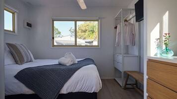 A bedroom with a bed, a window, a ceiling fan, a wardrobe, and a bench.
