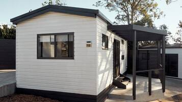 A small, single-story mobile home with a gabled roof, a front porch, and a number '12' sign.