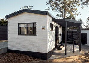 Une petite maison mobile d’un seul étage, dotée d’un toit à pignon, d’un porche à l’avant et d’une plaque portant le numéro « 12 ».