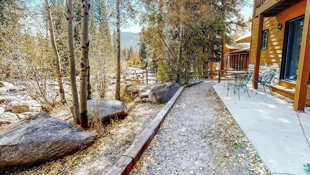 Une cabane en bois dotée d’un patio, entourée d’arbres et bordée d’un chemin de gravier.