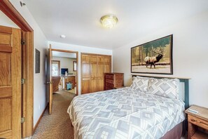 A bedroom with a bed, wooden wardrobe, a painting of an elk, and a desk with a chair. - Riverfront condo with free wifi, fireplace, patio, & gas grill (Grand Lake)