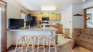 Une cuisine avec des meubles en bois, un îlot central doté de tabourets, une télévision et un four à micro-ondes.