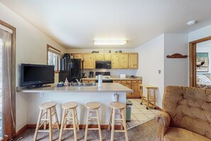A kitchen with wooden cabinets, a central island with stools, a television, and a microwave. - Riverfront condo with free wifi, fireplace, patio, & gas grill (Grand Lake)
