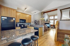 Eine Küche mit Granit-Arbeitsplatten, Holzsäulen, einem schwarzen Kühlschrank und einer Stein-Kochinsel mit Barhocker.
