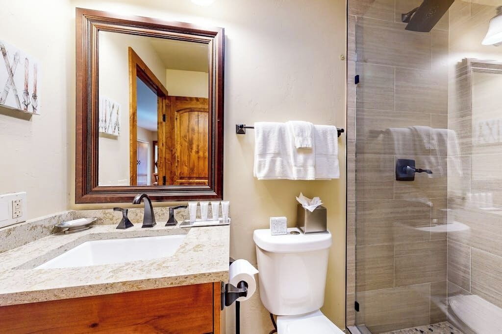 A bathroom with a sink, mirror, toilet, and shower.