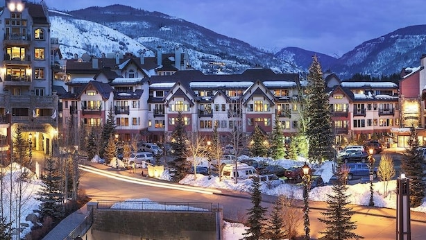 A hotel with multiple buildings, a parking area, and snow-covered mountains in the background. - Ski-in/out, riverfront studio w/ alpine view, fast WiFi, shared pool/hot tubs/WD (Vail)