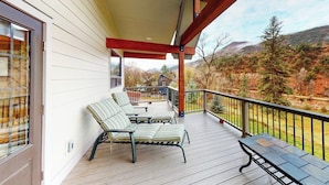 A covered porch with a wooden deck, a seating area with striped cushions, and a view of a mountainous landscape. - Two-level home on one acre w/ mountain views and deck on Crystal River (Carbondale)