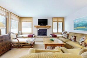 Ein Wohnzimmer mit Kamin, einem an einer Holzregal montierten Fernseher und einer Couch mit gemusterten Kissen.