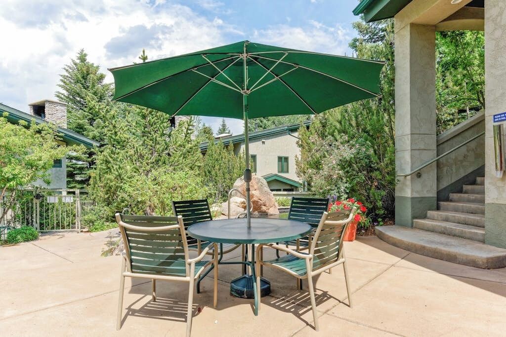 An outdoor patio with a round table and chairs, a green umbrella, and a staircase.
