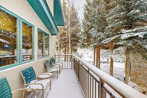 Ein mit Schnee bedeckter Balkon mit Sitzgelegenheit und Geländer, im Hintergrund schneebedeckte Bäume.