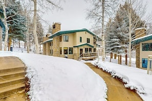 Ein zweistöckiges Haus mit Natursteinfassade, einem grünen Dach und einer Veranda.