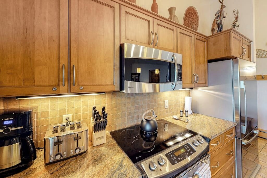 Una cocina con armarios de madera, un microondas de acero inoxidable, una estufa a gas, una cafetera y un tostador.