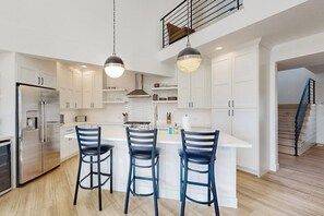Eine moderne Küche mit weißen Schränken, einem Edelstahlkühlschrank und drei blauen Barhocker.
