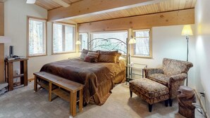 A bedroom with a bed, bench, armchair, and bedside table.