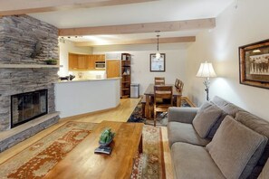 A living room with a stone fireplace, a wooden coffee table, a sofa, and a dining area with a table and chairs.