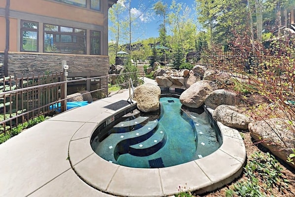 A swimming pool with a unique design, surrounded by rocks and greenery, with a building in the background.