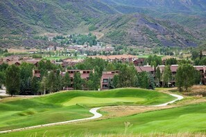 Ein Golfplatz mit gewundenem Weg, umgeben von Gebäuden mit roten Dächern und einer Bergkulisse.