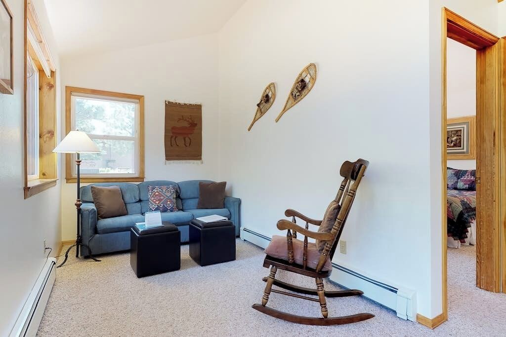 A living room with a blue sofa, two ottomans, a rocking chair, a lamp, and wall art.