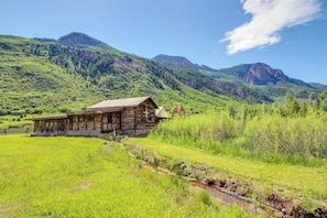 Eine rustikale Holzhütte mit geneigtem Dach, umgeben von üppigen grünen Feldern und Bergen.