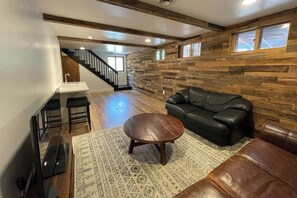 Ein modernes Wohnzimmer mit einer Holzwand, einem schwarzen Ledersofa, einem runden Couchtisch und einer Treppe, die zu einer oberen Ebene führt.