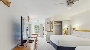 Una habitación de hotel con cama, escritorio, computadora, televisor y ventilador de techo.