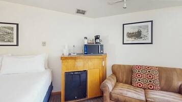 Une chambre d’hôtel avec un lit, une petite kitchenette équipée d’un four à micro-ondes et d’un réfrigérateur, un canapé en cuir marron et deux tableaux encadrés accrochés aux murs.