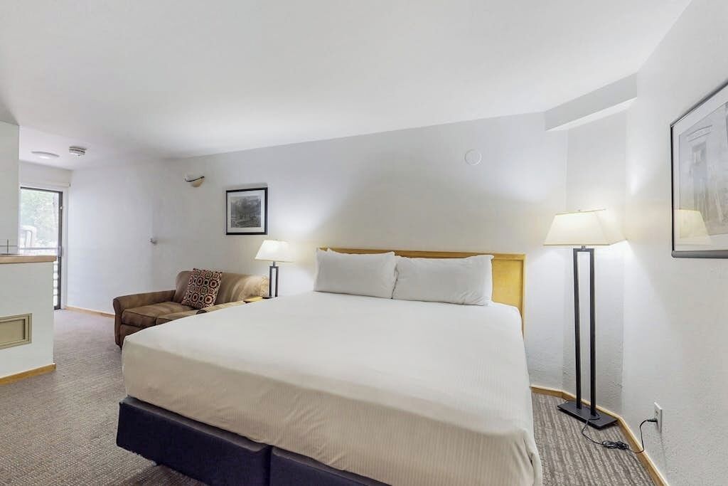 A hotel room with a large bed, two bedside lamps, a chair, and a desk.