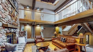 A spacious living area with a stone wall, leather furniture, and a staircase. - Main Street stay - pool & hot tub - walk to lifts, dog-friendly, ground-floor (Aspen)