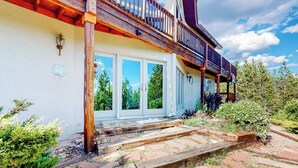 Un balcone in legno con ringhiera, un insieme di porte finestre e un viale di pietra che conduce all'ingresso.