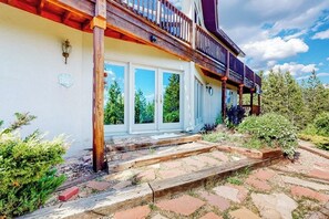 Ein Holzbalkon mit Geländer, doppelte Türen und ein Steinweg, der zum Eingang führt.