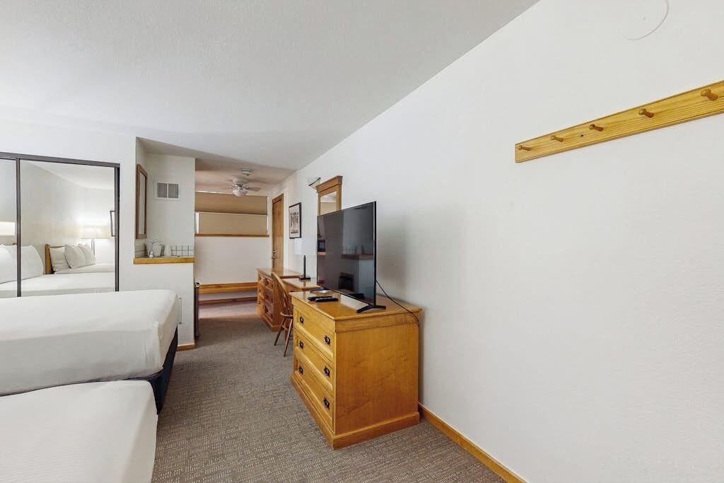 A hotel room with two beds, a TV, a wooden dresser, and a mirror on the wall.