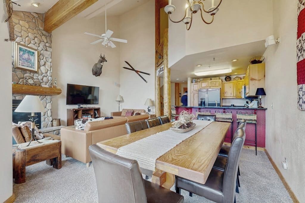 Een ruime woonkamer met een lange eettafel, een open haard, een televisie en een keuken op de achtergrond.