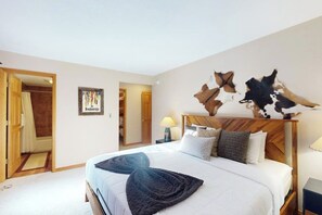 Ein Schlafzimmer mit einem großen Bett, einem Holzkopfstück, einem Wandbild und einer Tür zu einem anderen Raum.