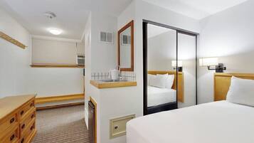 Una camera d'albergo con un letto, una cassettiera, uno specchio, una finestra con tende e una porta.