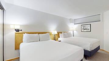 Una camera d'albergo con due letti, una testiera in legno, lampade sui comodini, un quadro appeso al muro e un pavimento con moquette.