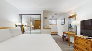 Hotellihuone, jossa on suuri sänky, työpöytä tuolilla, televisio ja peili.