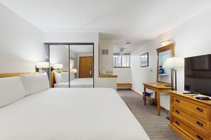 A hotel room with a large bed, a desk with a chair, a television, and a mirror.