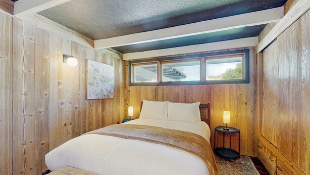 A wooden-paneled bedroom with a large bed, two bedside lamps, and a window with a view.