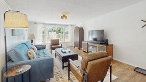 A modern living room with a sofa, armchair, ottoman, TV stand, and a lamp.