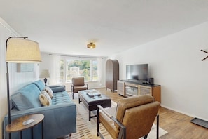 Ein modernes Wohnzimmer mit einer Couch, einem Sessel, einem Hocker, einer TV-Konsole und einer Lampe.