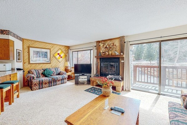 A living room with a sofa, TV, fireplace, and a balcony with a railing. - Stunning 1st-floor ski-in condo with hot tubs, fireplace, & gym (Breckenridge)