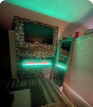 Ein Zimmer mit Wandmuster, einem Flachbildfernseher und einem eingebauten Kamin mit roten und grünen Lichtern.